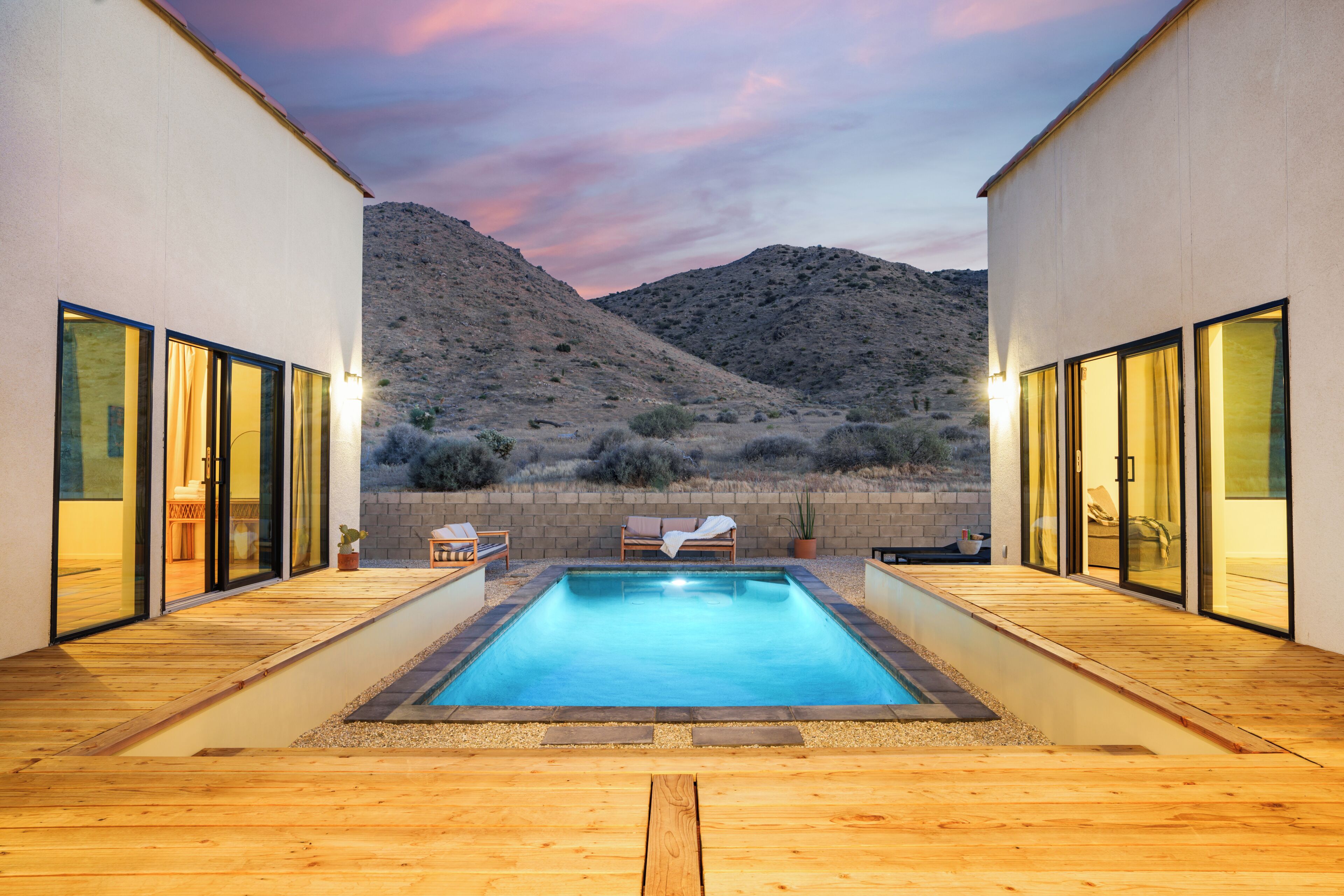 Ein moderner Pool mit Holzterrasse, Glasüren und Blick auf eine Berglandschaft.