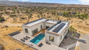 Una moderna casa a due piani con piscina, circondata da vegetazione desertica.