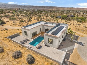 Ein modernes, zweistöckiges Haus mit Swimmingpool, umgeben von Wüstenpflanzen.