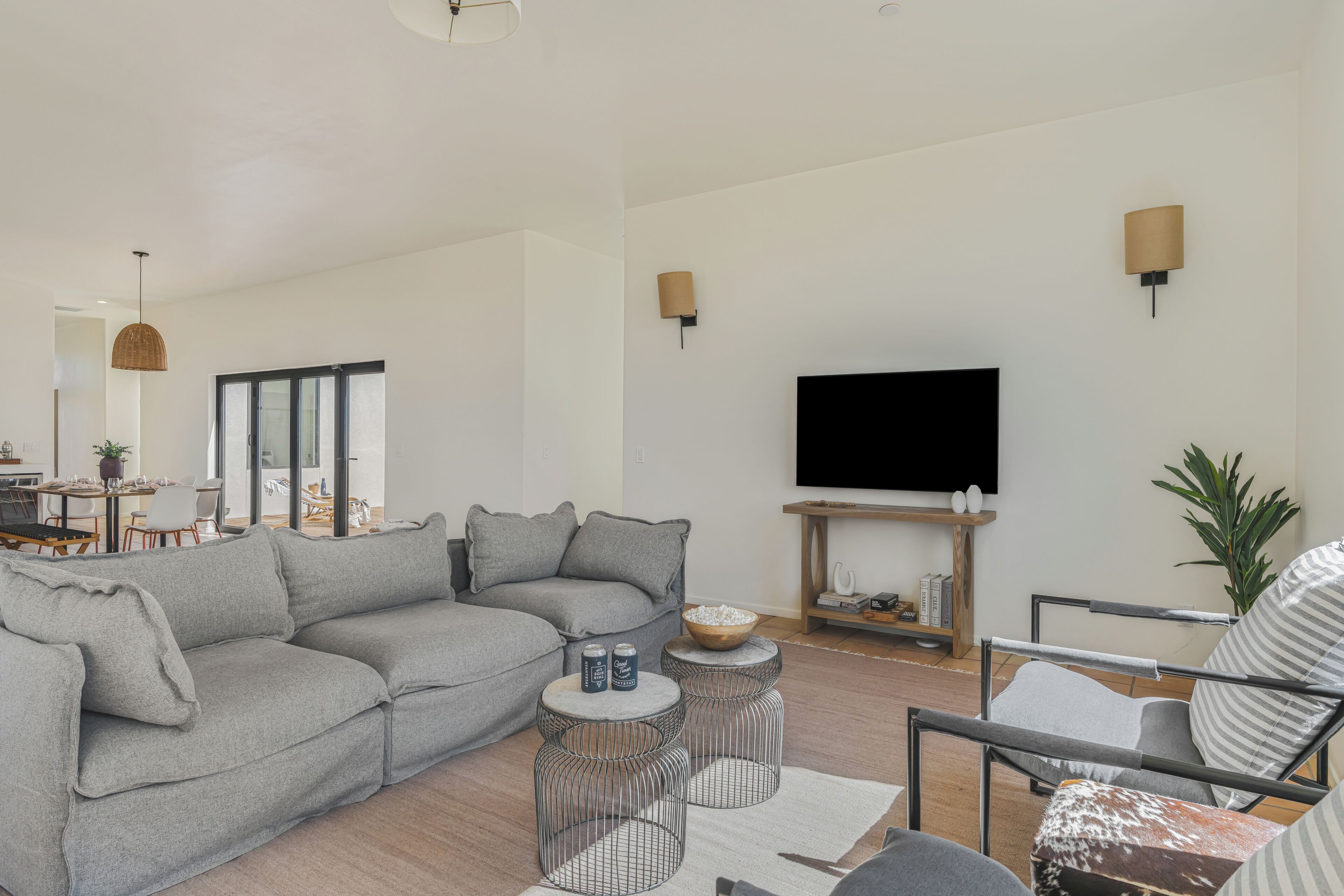 A modern living room with a grey sofa, a coffee table, a TV, and a dining area in the background.