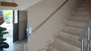 Una escalera con barandilla, una puerta con letrero y una planta.