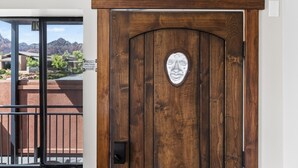 Una puerta de madera con un emblema de metal, un balcón con barandilla de metal y vistas a edificios y montañas al fondo.