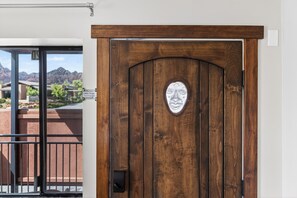 Eine Holztür mit einem Metallzeichen, ein Balkon mit Metallgeländer und im Hintergrund eine Aussicht auf Gebäude und Berge.