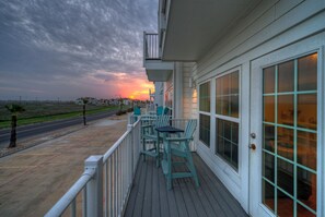 Ein Balkon mit Stühlen und Tisch, mit Blick auf eine Straße und einen Sonnenuntergang.