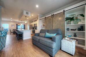 Ein modernes Wohnzimmer mit grauem Sofa, Holzboden, einer Küche im Hintergrund und einem Schiebetürenschrank im Stil einer Scheune.