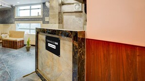 A reception area with a marble counter, a wooden bench, and a sign indicating it is serviced by a company. - Townhouse Oak Panki Panchmukhi Hanuman (Kanpur)