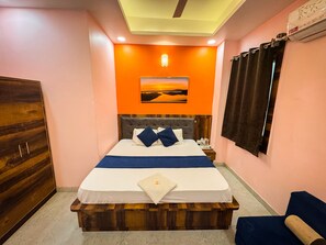A bedroom with a bed, a wooden headboard, a nightstand, a wall-mounted air conditioner, and a painting above the bed. - Maa Durga Dham (Vrindavan)