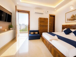 A modern bedroom with a large bed, a seating area, and a TV. - Maa Durga Dham (Vrindavan)