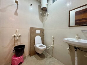 A bathroom with a toilet, a sink, a shower, and a bucket. - Maa Durga Dham (Vrindavan)