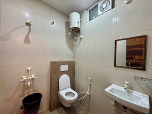 A small bathroom with a toilet, a sink, a mirror, a showerhead, and a water heater. - Maa Durga Dham (Vrindavan)