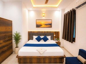 A modern hotel room with a large bed, a wooden wardrobe, a potted plant, and a painting of a sunset. - Maa Durga Dham (Vrindavan)