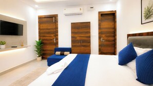 A modern bedroom with a bed, a flat-screen TV, wooden wardrobes, and an air conditioning unit. - Maa Durga Dham (Vrindavan)