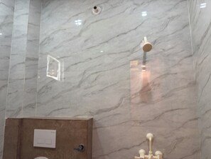 A bathroom with a marble wall, a wooden cabinet, and a shower with a handheld showerhead. - Maa Durga Dham (Vrindavan)