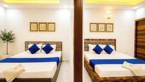 A hotel room with two beds, a potted plant, and framed artwork on the wall. - Maa Durga Dham (Vrindavan)