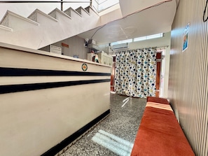 Un vestíbulo de hotel con un letrero de recepción, un mostrador de atención al cliente, una cortina estampada y una alfombra roja.