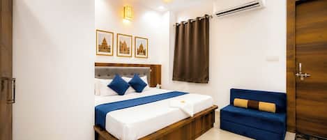 Une chambre d’hôtel avec un lit, un canapé bleu, un ventilateur de plafond, un appareil de climatisation et des tableaux encadrés accrochés au mur.