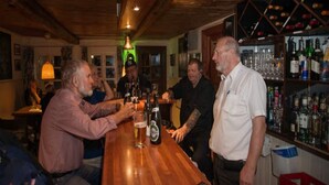 En bar med træbjælker, bardisk og hylder med flasker.