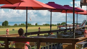 En terrasse med udendørs siddepladser, parasoller og havudsigt.