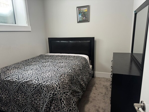 A bedroom with a bed, a dresser, a window, and a painting on the wall.
