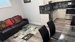 Een moderne keuken met een zwart aanrecht, roestvrijstalen apparatuur en een eethoek met een glazen tafel en zwarte stoelen.