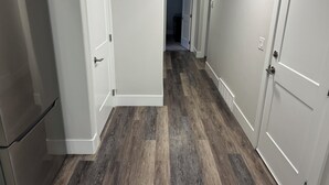 Een gang met houten vloer, witte muren en deuren die naar andere kamers leiden.