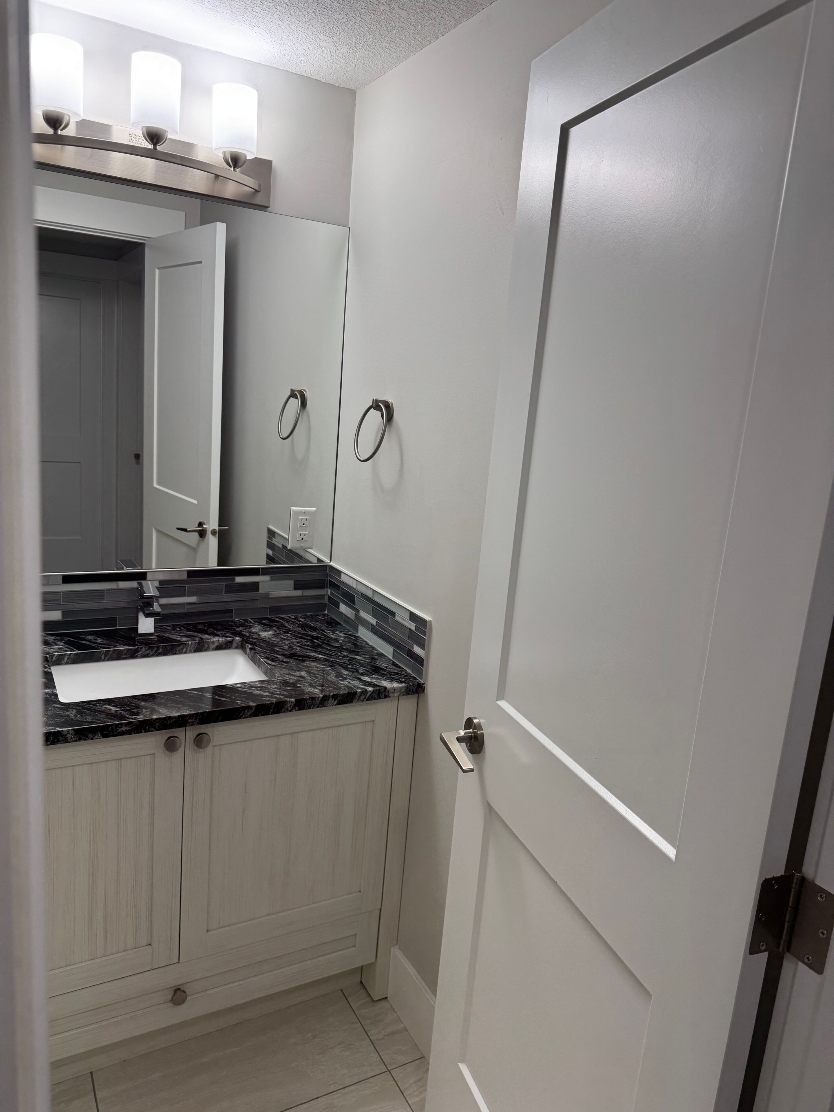 A bathroom with a marble countertop sink, a mirror, and a door with a handle.