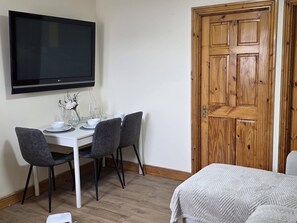 A room with a dining table set for two, a television mounted above it, and a wooden door.