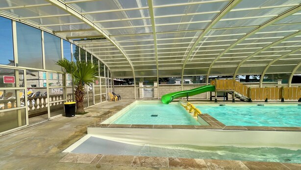 Piscina interna com escorregador, paredes de vidro e uma palmeira.
