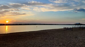 Uma praia com um pôr do sol, águas calmas e uma estrutura com telhado.