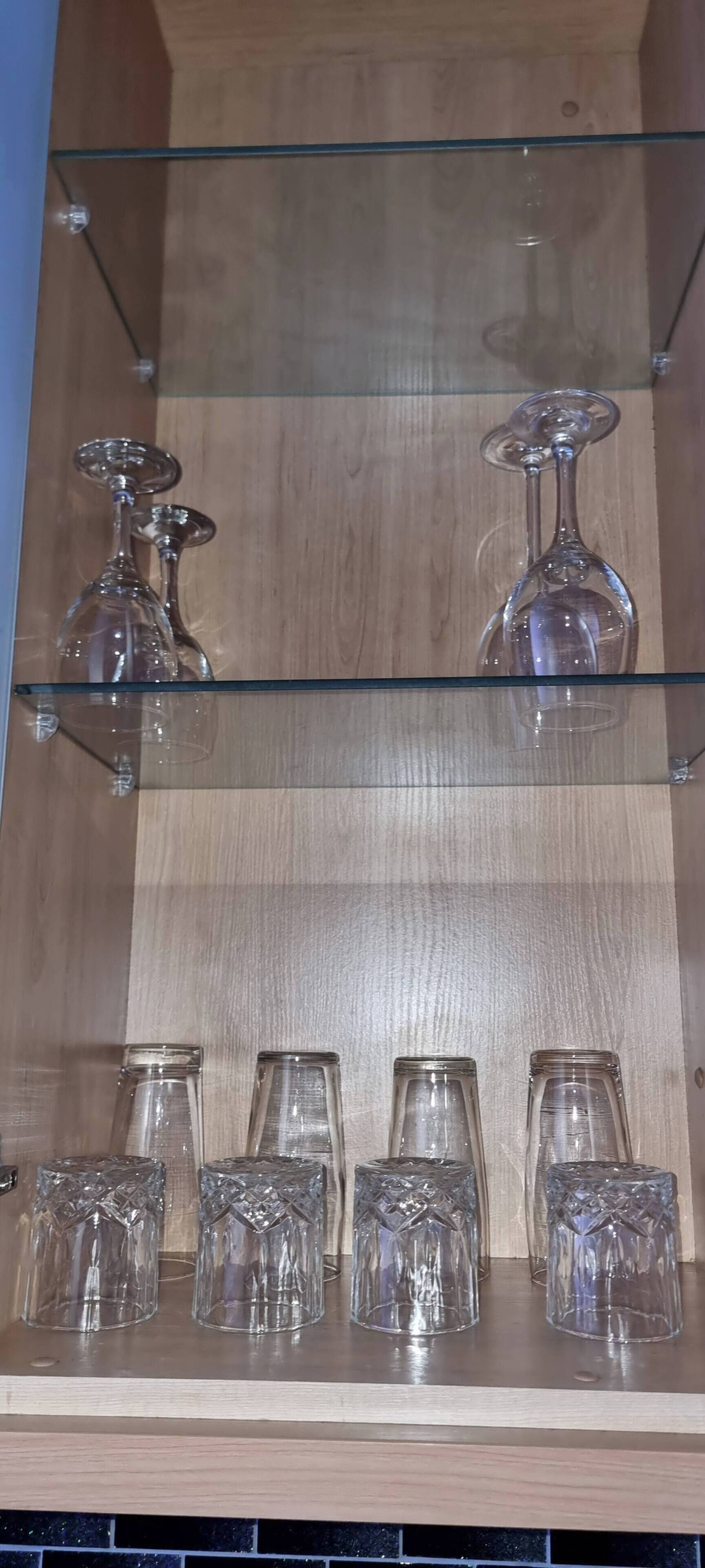 Une étagère en bois sur laquelle sont disposés des verres, notamment des verres à vin et des verres à cocktail en cristal.