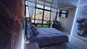A bedroom with a bed, a TV, a window with curtains, and a view of the outdoors. - Waterfront Deco apartment 2 sleeper lake views (Cape Town)