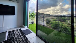 Un salon moderne doté d’une grande porte vitrée donnant sur un balcon qui offre une vue sur un paysage verdoyant et un ciel nuageux.