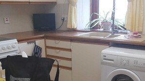Ett litet pentry med en tvättmaskin, ett bord med en väska på och ett fönster med gardiner.