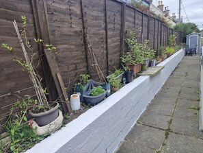 A narrow pathway flanked by a wooden fence and various potted plants. - Spacious 3 Bedroom House with outdoor patio area for outdoor dining and WIFI (Portknockie)