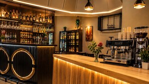 Una zona de bar con mostrador de madera, estantes llenos de botellas de licores, una máquina de café y una planta en maceta.