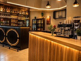 A bar area with a wooden counter, shelves of liquor bottles, a coffee machine, and a potted plant.