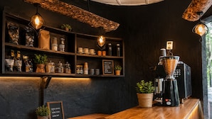 Interior de una cafetería con estantes llenos de sacos de café, una máquina de café y una pizarra de menú.