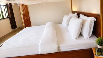Una cama bien hecha con sábanas blancas, un cabecero de madera y una mesita de noche con un control remoto y una planta en maceta.
