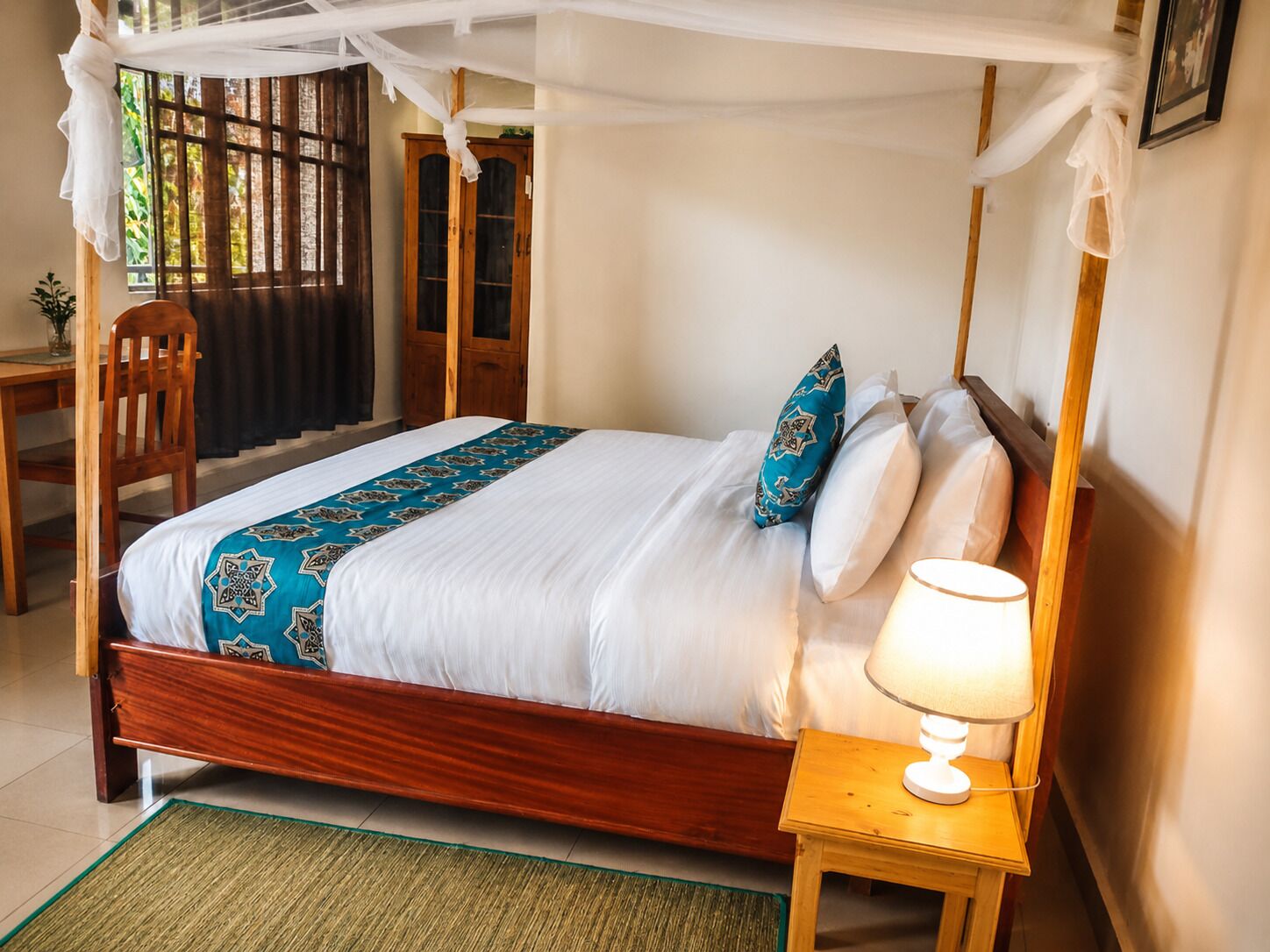 A bed with a canopy, a bedside lamp, and a view of a wooden door and window.
