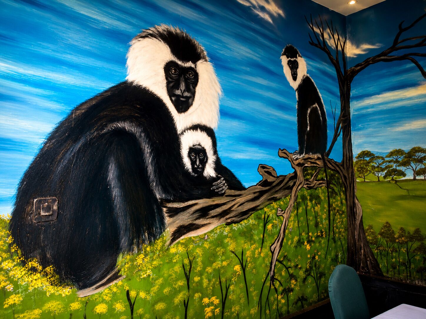 A mural of a large black and white primate on a tree branch with a smaller primate below it, set against a backdrop of a blue sky and green landscape.
