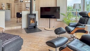 Un salon moderne avec une cheminée, des fauteuils en cuir, un téléviseur à écran plat et un plancher en bois.