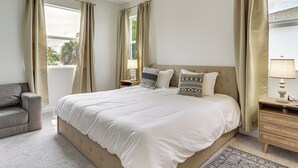 Une chambre à coucher avec un grand lit, deux tables de chevet, une chaise et des rideaux.