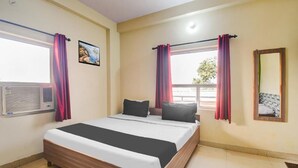 A hotel room with a bed, curtains, a window, an air conditioning unit, a wall-mounted mirror, and a framed picture. - Hotel Radhe Radhe Near Jaipur Airport  (Jaipur)