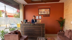 A reception area with a receptionist, a wooden reception desk, two sofas, a coffee table, and a large window. - Hotel Radhe Radhe Near Jaipur Airport  (Jaipur)