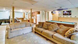 A living room with a pool table, two sofas, a kitchen area, and a pool. - Classic Up North Cabin: Boat, Fish, ATV & Explore (Harrison)