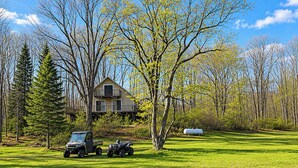 A house with a large yard, surrounded by trees and a clear sky. - Classic Up North Cabin: Boat, Fish, ATV & Explore (Harrison)