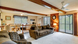 A cozy living room with a couch, a dining area with a table and chairs, a ceiling fan, and a large window. - Classic Up North Cabin: Boat, Fish, ATV & Explore (Harrison)