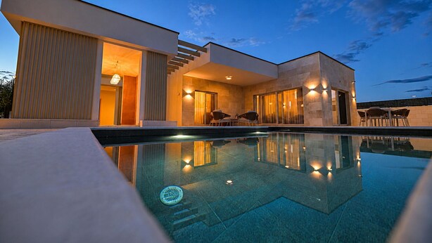 Une maison moderne dotée d’une piscine, de grandes fenêtres et d’un espace salon extérieur.