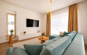 A modern living room with a large sofa, a flat-screen TV, a radiator, and a window with curtains. - Awesome home in Smokovic with sauna (Smokovic)