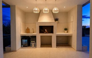 A modern kitchen with a built-in fireplace, pendant lights, and a view of the outdoors. - Awesome home in Smokovic with sauna (Smokovic)